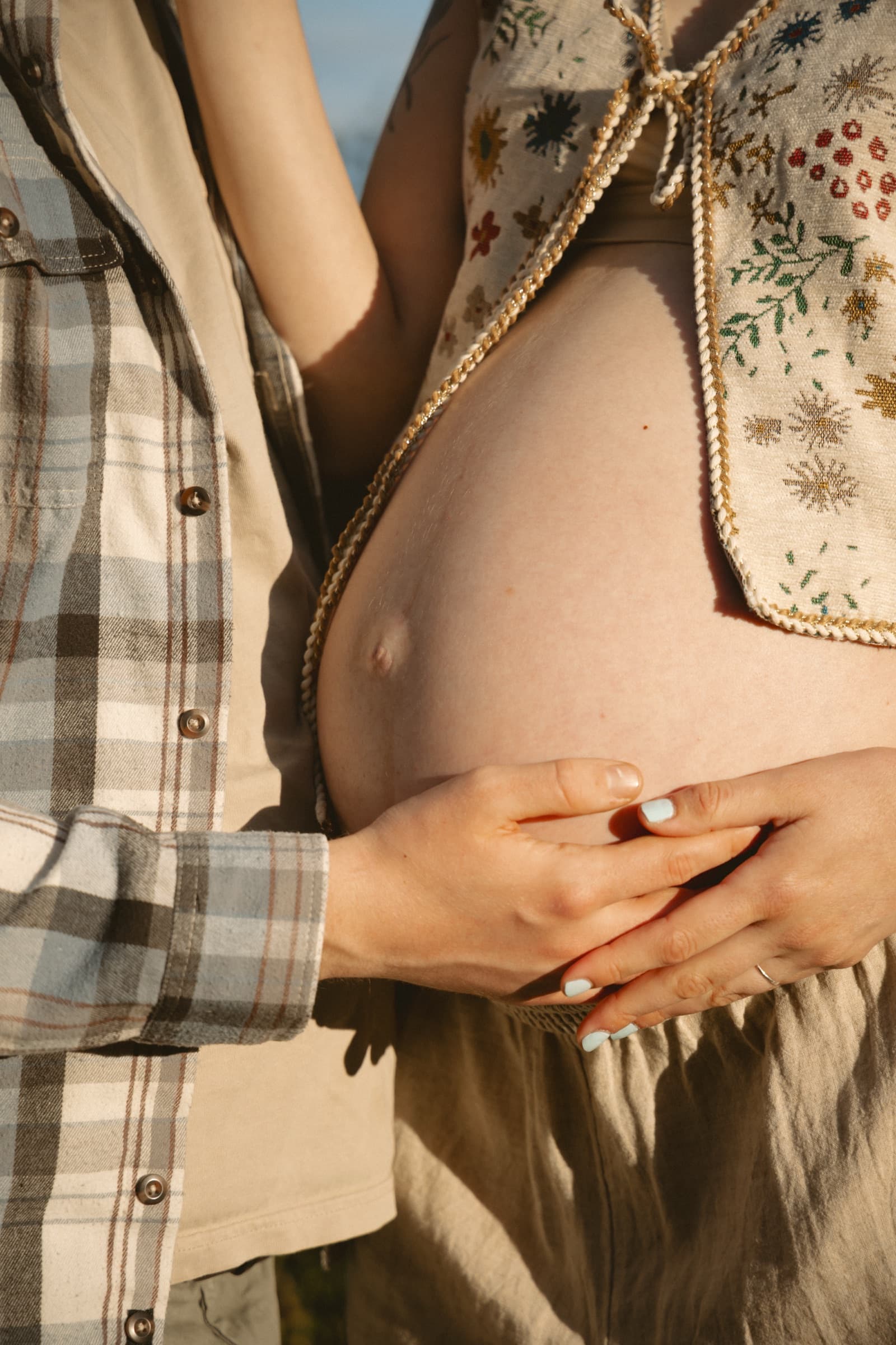 A pregnant person cradling their belly in warm evening light
